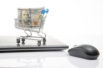 Model of a grocery cart with dollar money on the background of a laptop. Online business sale. Financial business success.