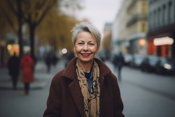 Fototapeta premium Portrait of a smiling senior woman in the city. She is wearing a coat.
