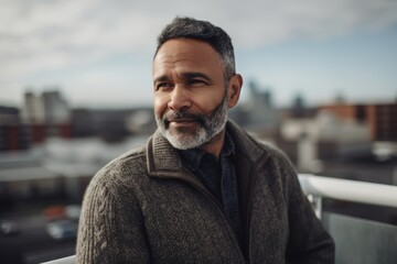 Portrait of a handsome mature man with grey hair and beard wearing a coat, looking at the camera and smiling while standing on a rooftop terrace