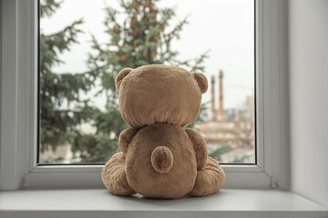 Cute lonely teddy bear on windowsill indoors, back view