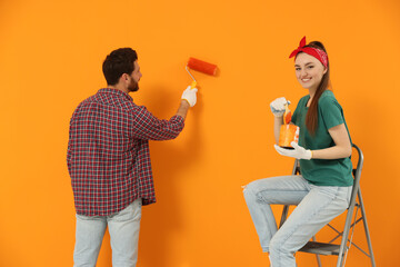 Man painting orange wall and happy woman holding can of dye with brush. Interior design