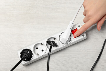 Woman pressing button of power strip on white wooden floor, top view. Space for text