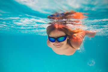 Fototapeta premium Child dives into the water in swimming pool. little kid swim underwater in pool. Child swimming underwater in sea or pool water. Summer vacation fun. Underwater portrait cute kid in swimming pool.
