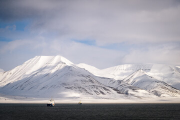 2022-05-09 SNOW COVERED MOUNTAIN RANGE WITH NICE SMOOTH CLOUDS AND TWO COMMERICAL SHIPS IN THE SEA NEAR SVALABRD NORWAY IN THE ARCTIC