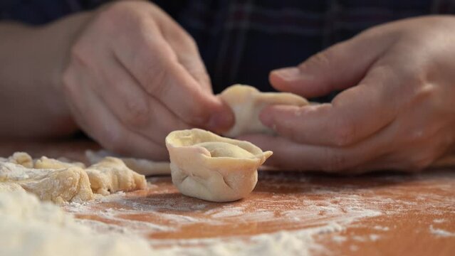 Male person puts forcemeat as filling for homemade dumplings on wooden table. Houseman prepares tasty dumplings for dinner in blurry kitchen