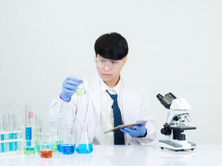 Asian man student scientist Wearing a doctor's gown in the laboratory, looking at the results through a microscope. on a table in a scientific research laboratory with test tubes on a white table