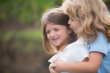 Fototapeta premium Adorable happy kids outdoors on summer day, little boy kissing a girl. Lovely little boy and girl, have fun and hugging outdoor. Funny kids face. Kids playing in spring park.