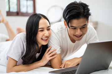 Asian attractive woman using laptop on bed with husband in the morning. 