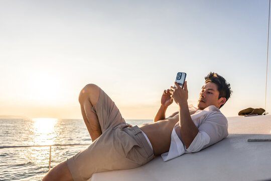 Asian young man tourist using smartphone taking photo during yachting. 