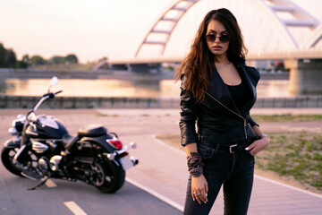 Attractive curly hair brunette in leather jacket standing in front her motorcycle 