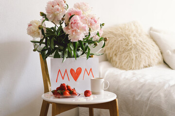 Breakfast for Mothers Day. Heart shaped white plate with fresh strawberries, cup of coffee, gift and Peonys bouquet with gift in bed. Still life composition. Happy Mother's Day.