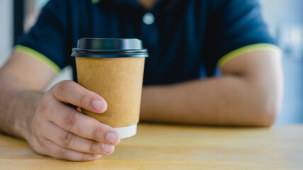 Man hand holding brown paper cup with black lid of hot coffee in coffee cafe. Take away hot drink.