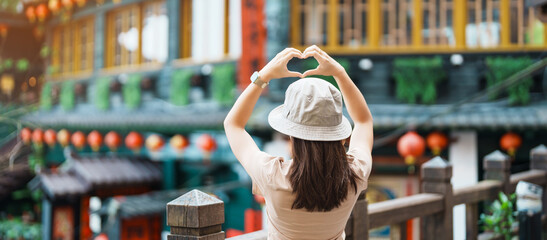 woman traveler visiting in Taiwan, Tourist with hat sightseeing in Jiufen Old Street village with Tea House background. landmark and popular attractions near Taipei city . Travel and Vacation concept