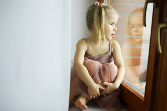 Beautiful little girl smiling and watching out the window. A child looks out the window. Young girl looking from window.