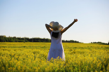 Pretty girl with a hat in her hand walks in a field with field flowers and smiles sincerely