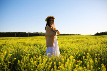 Fototapeta premium Pretty girl with a hat in her hand walks in a field with field flowers and smiles sincerely