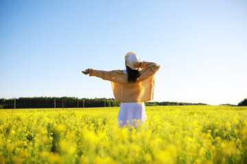 Pretty girl with a hat in her hand walks in a field with field flowers and smiles sincerely