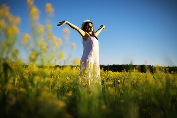 Pretty girl with a hat in her hand walks in a field with field flowers and smiles sincerely