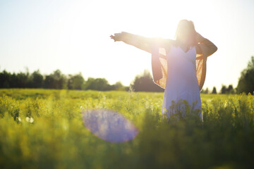 Pretty girl with a hat in her hand walks in a field with field flowers and smiles sincerely