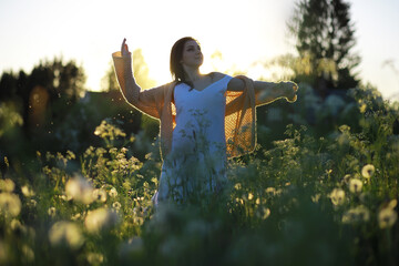 Pretty girl with a hat in her hand walks in a field with field flowers and smiles sincerely