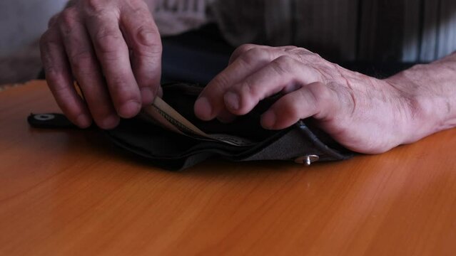hands of an old man opening an old wallet in which the last dollar bills remained. selective focus. a beggarly existence in old age, bankruptcy and the need for old age