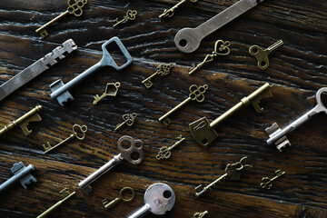A lot of metal keys and a steel lock on a wooden boards. Vintage rusty padlock surrounded by old...
