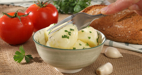 boiled potatoes prick with a fork in a bowl. farm products on the table. simple country food. potato dish with tomatoes and bread on burlap. natural food on a sunny day.