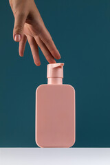 A woman's hand presses on a dispenser with a cosmetic product.