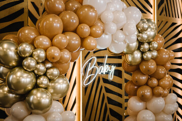 Arch decorated with brown, beige and golden balloons, text baby. Celebration baptism concept. Reception at birthday party on photo wall. Photo zone and location for celebration in the restaurant.