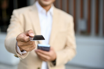 Close-up image of an Asian businessman in a business suit handing his business card to a camera.