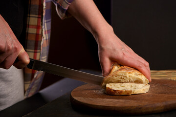 Whole grain bread put on kitchen wood plate with a chef holding knife for cut. The healthy eating and traditional bakery concept. Front viev. Fresh bread on table close-up