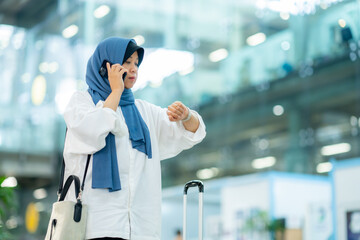 An Asian Muslim wearing a blue hijab is preparing for a vacation and she is at the airport. She is using her mobile phone to contact her friends and Muslim travelers.