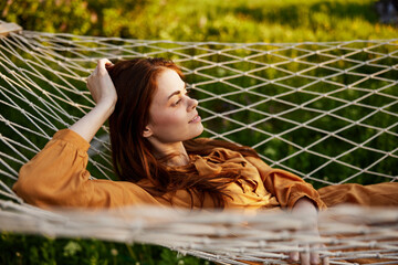 a happy woman is resting in a mesh hammock with her head resting on her hand, smiling happily...