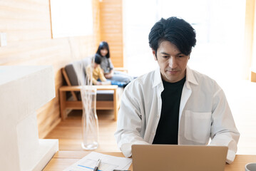 リモートワークをする日本人男性と後ろでくつろぐ子供たち