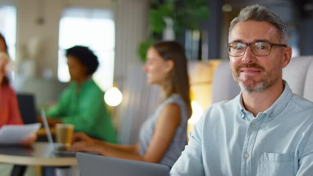 Portrait of mature businessman wearing glasses working on laptop in informal seating area of modern office on coffee break - shot in slow motion