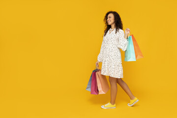 Young woman with shop bags on yellow background