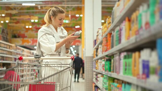 30s woman buy shampoo bottle. Girl choose hair gel. Lady take item put cart. Body care row. Customer read label beauty store. Buyer pick up lotion cosmetic shop. Blond person hold hand soap. Eco mall.