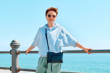 Strong woman leans on handrail along seaside promenade enjoying freedom at seaside. Female traveler relaxing in serene nature. Mental health, wellbeing, trip adventure and healthy lifestyle.