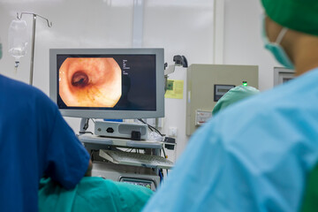 A doctor or surgeon in a light blue protective gown did a colonoscopy or gastroscopy inside operating theatre in the hospital.EGD technology for cancer screening.Blur green background and foreground. - obrazy, fototapety, plakaty