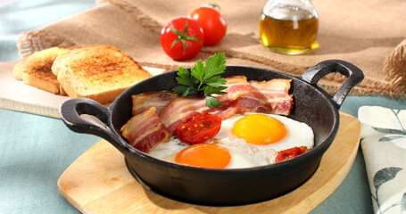 fried eggs with bacon and tomatoes in a frying pan. breakfast on the table. sunny morning. country style. organic farm food