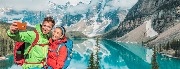 Couple travel selfie banner landscape happy hikers in winter alps lake view. Asian woman, Caucasian man using mobile phone