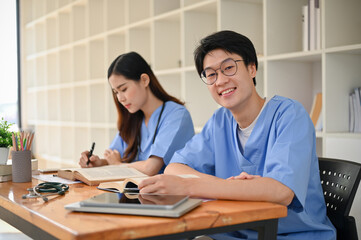 Obraz premium Handsome and smart young Asian male medical student in a uniform studying with his friend