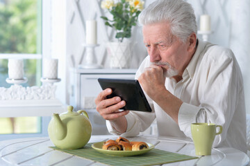 senior man using tablet while drinking tea
