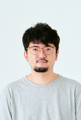 Obraz premium 白背景で眼鏡をかけた髭を生やしたカメラ目線の30代の1人の日本人男性の人物の上半身の正面