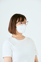 白背景でマスクと眼鏡を着けた右側を向いた30代の1人の日本人女性の人物の上半身