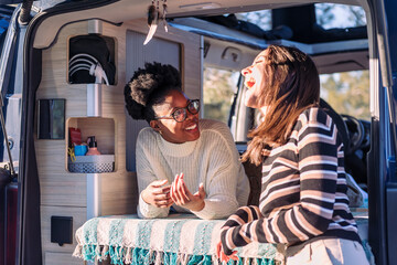 two happy women laughing in a conversation and enjoying van life, concept of weekend getaway with...