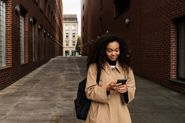 Beautiful african girl using smartphone while standing outdoors