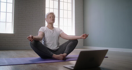 Mature caucasian woman doing yoga in studio. Senior woman relaxing in lotus position on floor,...