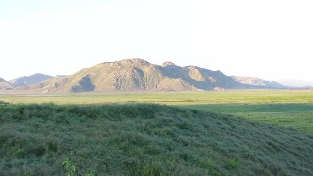 Slow pan drone flight reveals a valley of green grass and mountains.