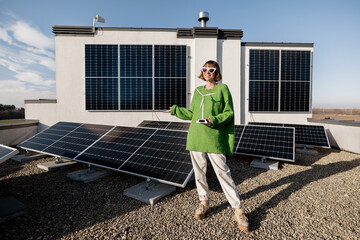 Portrait of a happy woman stands on a rooftop with a solar power plant installed on it. Happy owner...